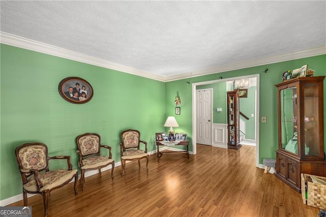 living area featuring baseboards, ornamental molding, a textured ceiling, and wood finished floors