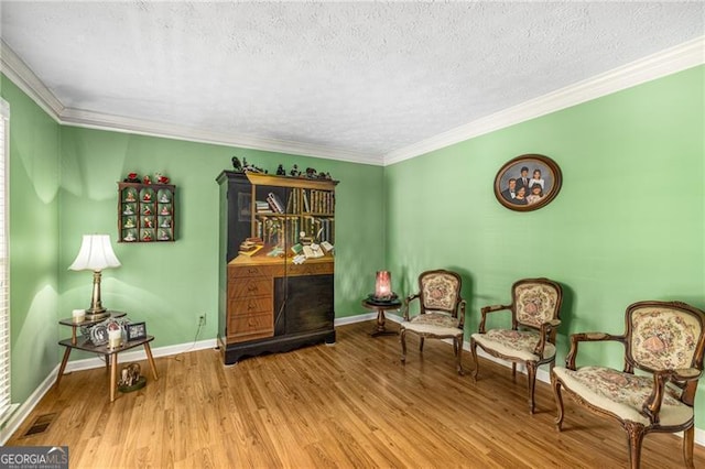 sitting room featuring crown molding, a textured ceiling, baseboards, wood finished floors, and visible vents