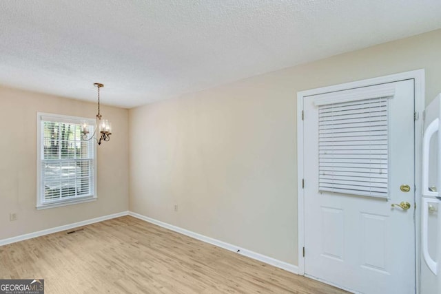 interior space featuring a textured ceiling, baseboards, a chandelier, and light wood-style floors