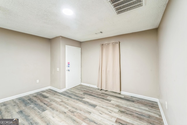empty room featuring visible vents, a textured ceiling, and wood finished floors