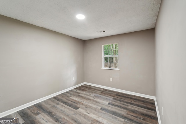 spare room with visible vents, a textured ceiling, baseboards, and wood finished floors