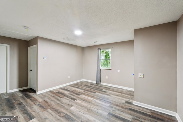 empty room with visible vents, a textured ceiling, baseboards, and wood finished floors