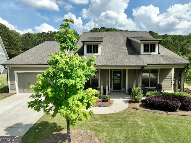 view of front of home with roof with shingles, an attached garage, a front yard, concrete driveway, and covered porch
