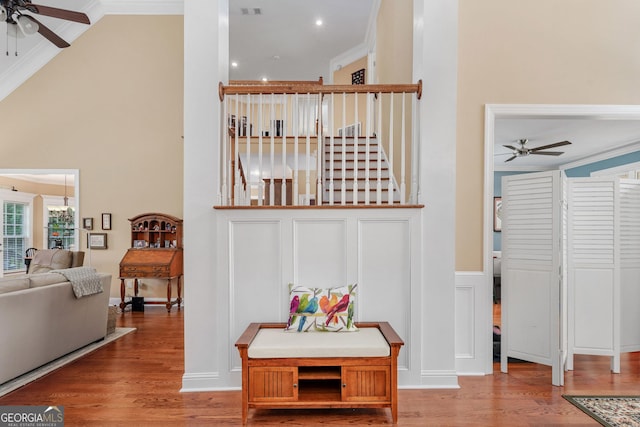 interior space with a high ceiling, ornamental molding, a ceiling fan, and wood finished floors