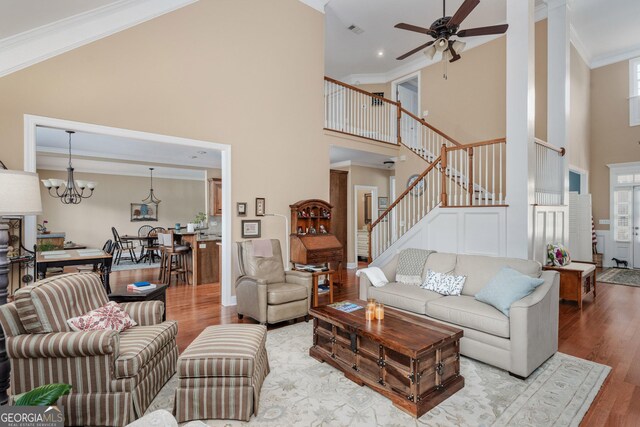 living room featuring stairs, a high ceiling, wood finished floors, and ceiling fan with notable chandelier