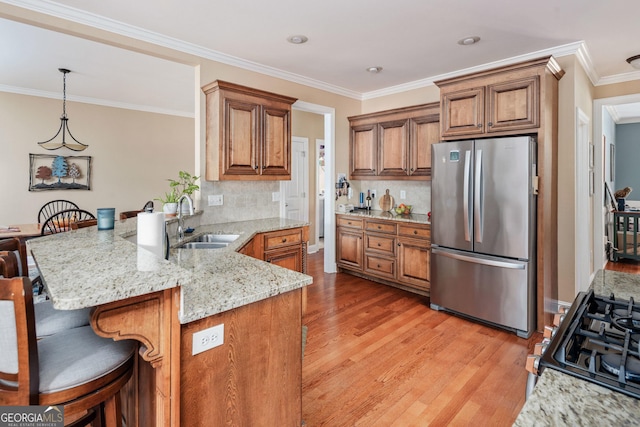 kitchen with brown cabinetry, freestanding refrigerator, a peninsula, a sink, and light wood finished floors