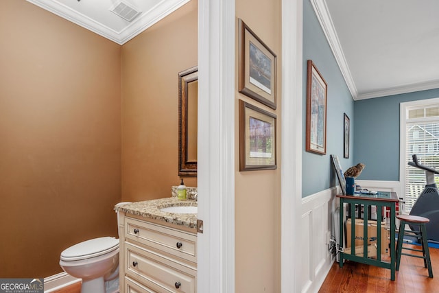 half bath featuring crown molding, vanity, toilet, wood finished floors, and visible vents