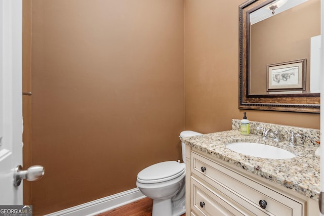 half bath with vanity, baseboards, wood finished floors, and toilet