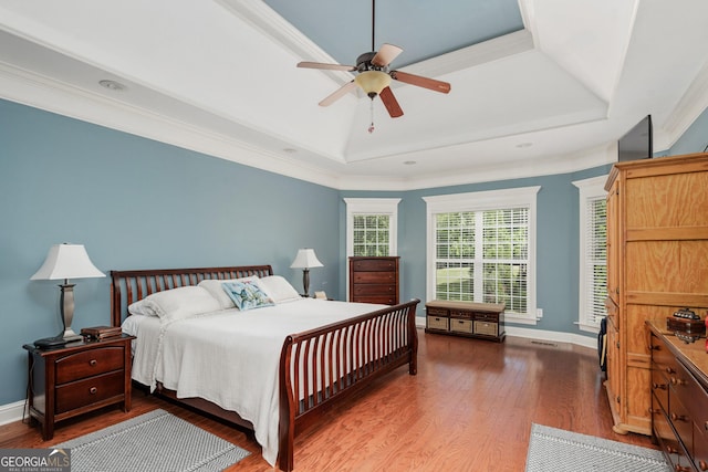 bedroom featuring baseboards, wood finished floors, and a tray ceiling