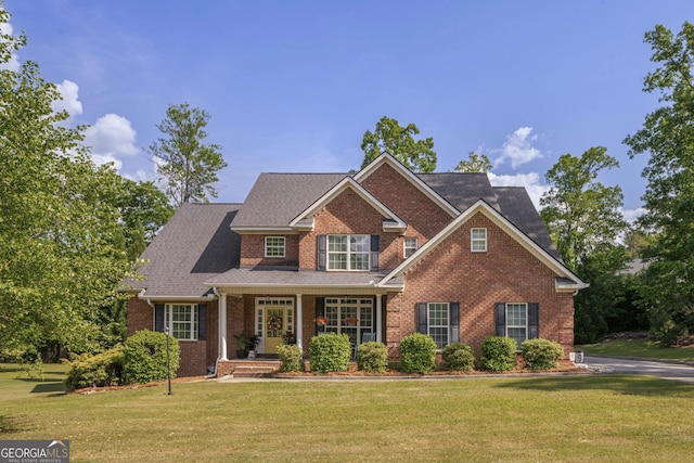 view of front facade featuring roof with shingles, covered porch, a front lawn, and brick siding