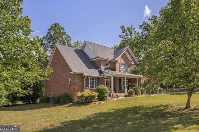craftsman-style house featuring roof with shingles, covered porch, a front yard, and brick siding