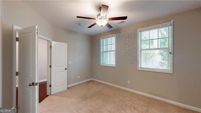 spare room featuring light colored carpet, ceiling fan, and baseboards