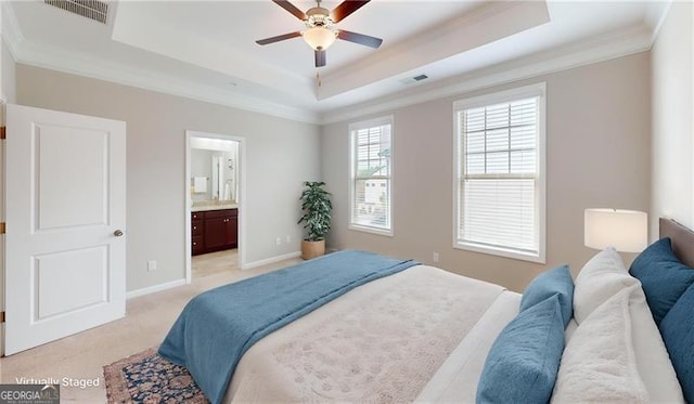 bedroom with a tray ceiling, ornamental molding, light colored carpet, ensuite bath, and baseboards