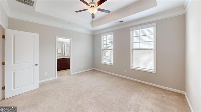 unfurnished bedroom featuring crown molding, a tray ceiling, light colored carpet, baseboards, and connected bathroom
