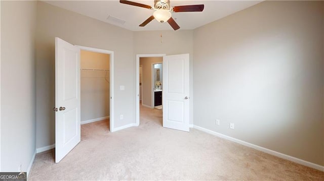 unfurnished bedroom with light carpet, a spacious closet, baseboards, a closet, and a ceiling fan