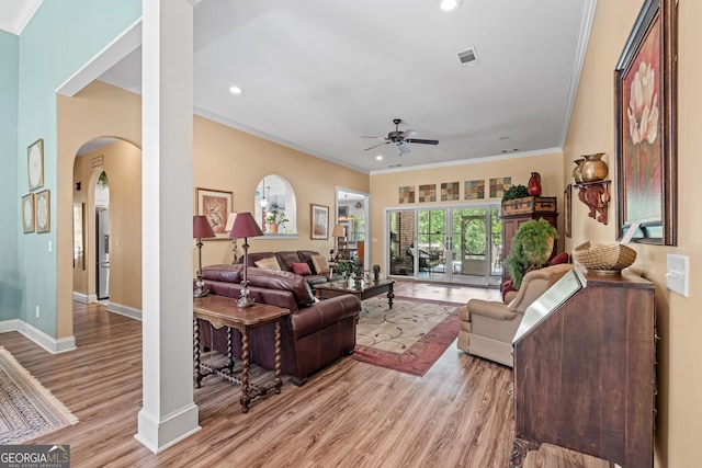 living room with ceiling fan, arched walkways, light wood-type flooring, visible vents, and ornamental molding