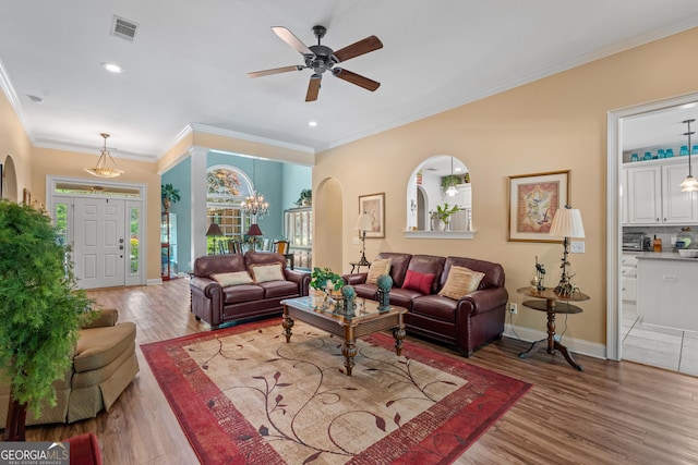 living room with visible vents, arched walkways, wood finished floors, baseboards, and ceiling fan with notable chandelier
