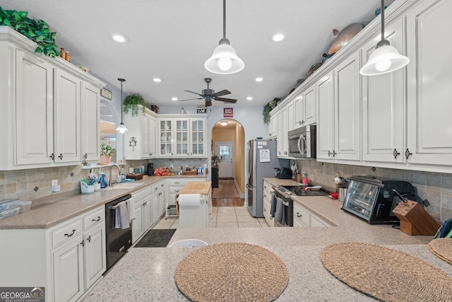 kitchen with ceiling fan, a sink, arched walkways, stainless steel appliances, and white cabinetry
