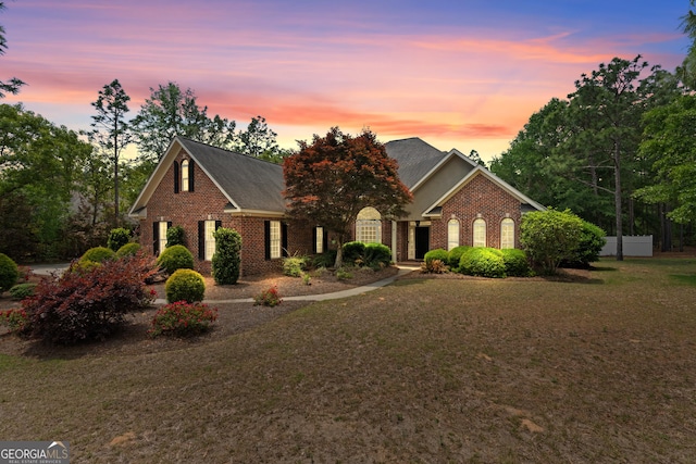 view of front of house featuring a shingled roof, a yard, and brick siding