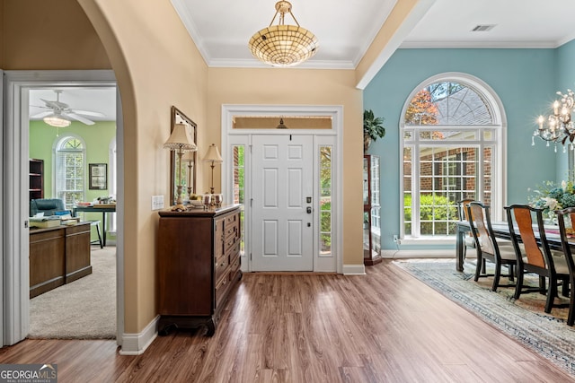 entryway featuring arched walkways, wood finished floors, baseboards, ceiling fan with notable chandelier, and ornamental molding