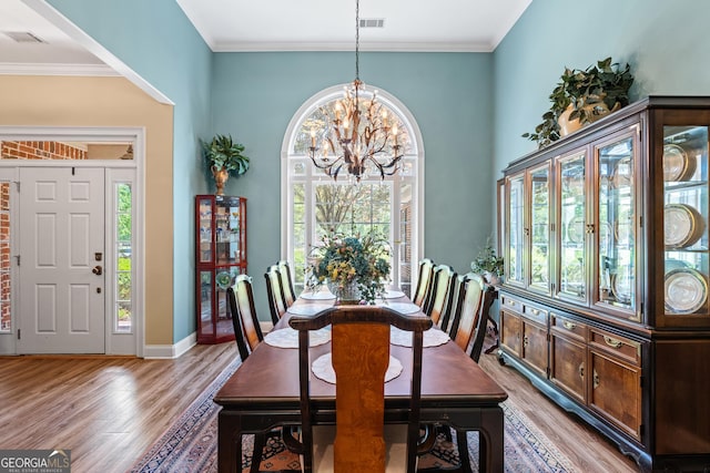 dining room featuring crown molding, a chandelier, light wood-style flooring, baseboards, and visible vents