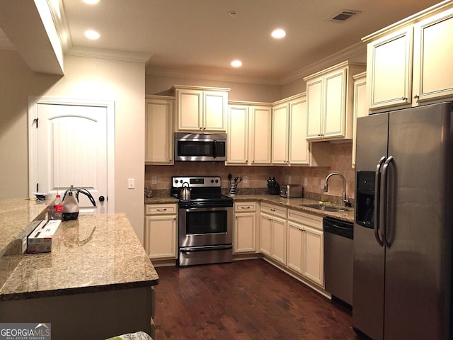kitchen with crown molding, cream cabinets, appliances with stainless steel finishes, a sink, and decorative backsplash