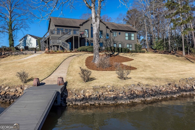 back of property featuring a deck with water view, stairs, and a lawn