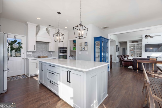 kitchen with dark wood-style flooring, visible vents, premium range hood, and appliances with stainless steel finishes