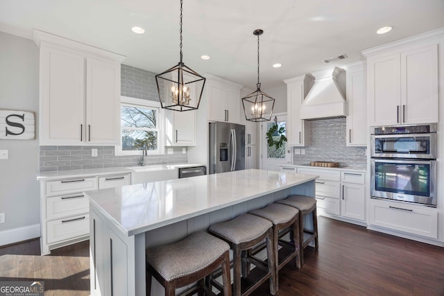 kitchen featuring a notable chandelier, visible vents, a sink, premium range hood, and stainless steel appliances