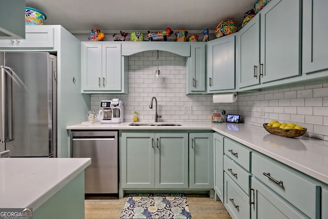 kitchen with stainless steel appliances, a sink, green cabinetry, light countertops, and decorative backsplash