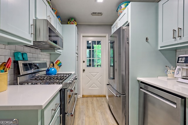 kitchen with appliances with stainless steel finishes, light wood-style floors, backsplash, and light countertops