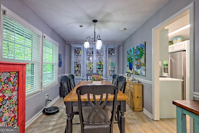 dining area featuring a chandelier, healthy amount of natural light, light wood-type flooring, and baseboards
