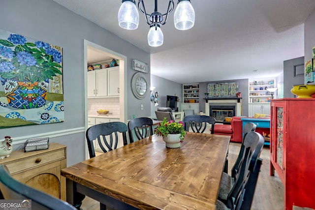 dining space with a glass covered fireplace, wood finished floors, built in shelves, and a chandelier