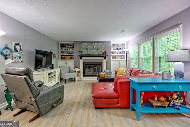 living room with wood finished floors, built in shelves, a glass covered fireplace, and a textured ceiling