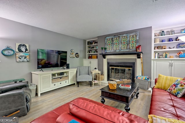 living area with a glass covered fireplace, a textured ceiling, wood finished floors, and built in features