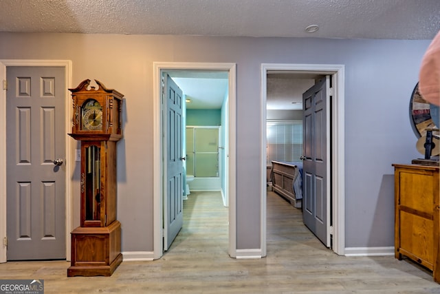 hallway with light wood-style flooring, a textured ceiling, and baseboards