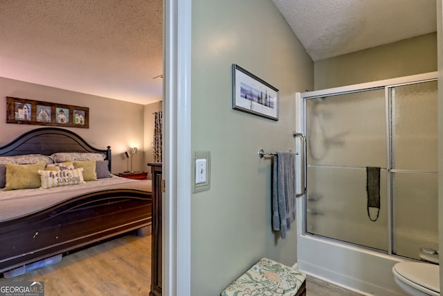 full bath with a textured ceiling, wood finished floors, combined bath / shower with glass door, and toilet