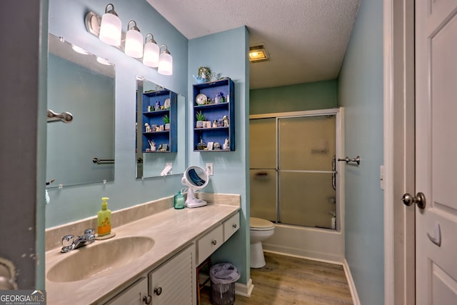 bathroom with wood finished floors, toilet, vanity, a textured ceiling, and combined bath / shower with glass door