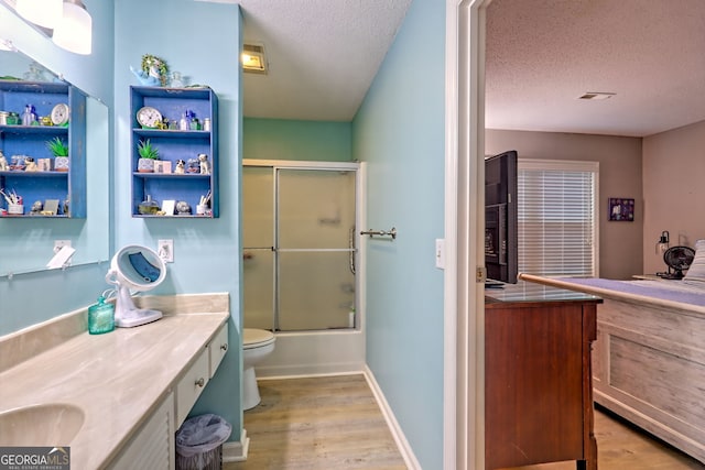full bath featuring vanity, wood finished floors, a textured ceiling, toilet, and enclosed tub / shower combo