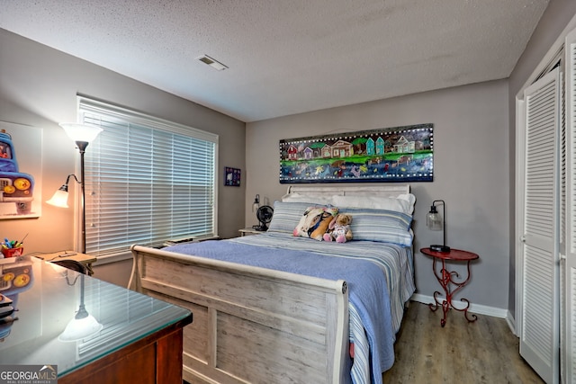 bedroom with wood finished floors, a closet, a textured ceiling, and baseboards
