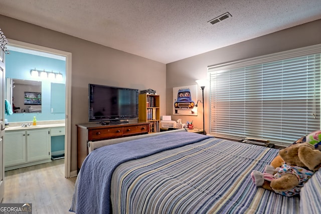 bedroom featuring light wood-type flooring, a textured ceiling, and connected bathroom
