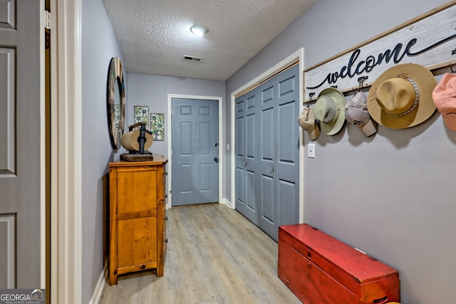 entryway with light wood-type flooring, a textured ceiling, and baseboards