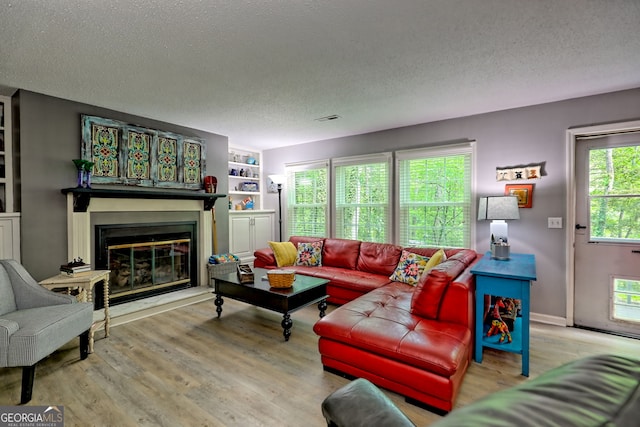 living area featuring a textured ceiling, wood finished floors, and a glass covered fireplace