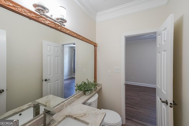 bathroom with ornamental molding, wood finished floors, toilet, a sink, and baseboards