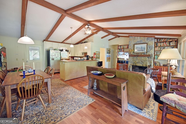 living area featuring ceiling fan, lofted ceiling with beams, light wood-type flooring, and a stone fireplace