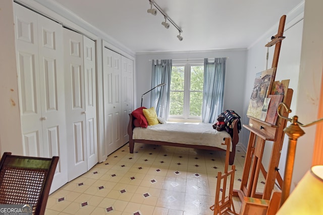 bedroom with crown molding, light tile patterned floors, two closets, and rail lighting