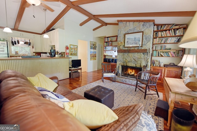 living area featuring a stone fireplace, lofted ceiling with beams, ceiling fan, and wood finished floors