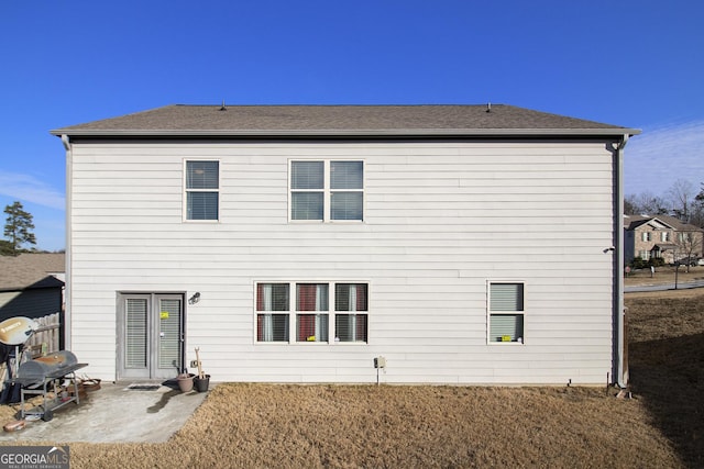 back of property with a lawn, a patio area, and roof with shingles