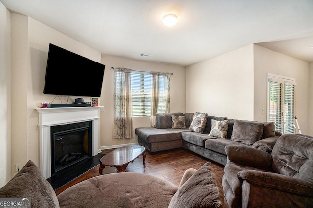 living room with dark wood-style flooring, baseboards, visible vents, and a fireplace with raised hearth