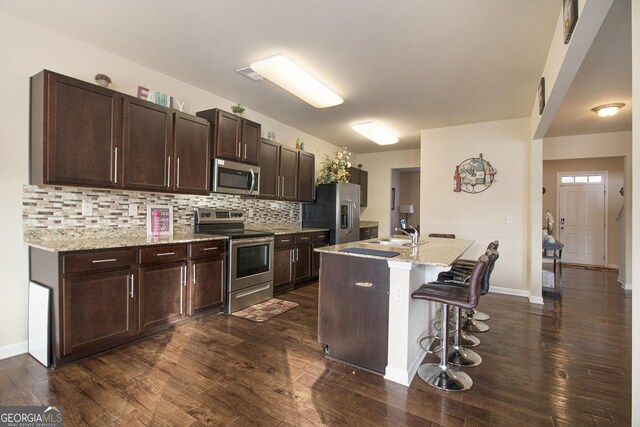 kitchen featuring a breakfast bar, dark wood-type flooring, a sink, appliances with stainless steel finishes, and backsplash